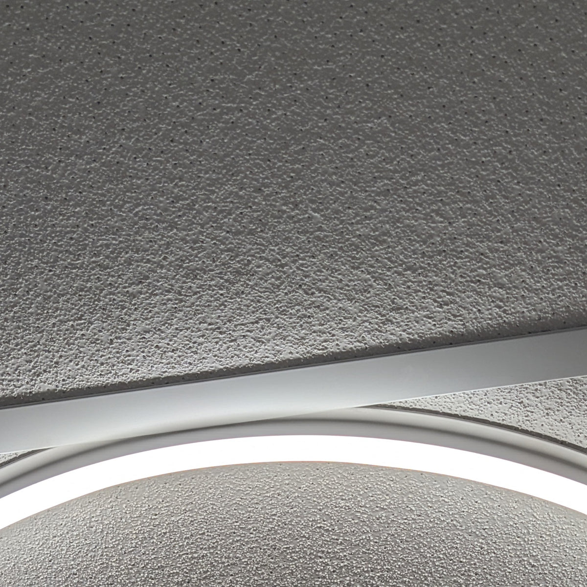 Close-up detail of the lit Round Halo ring, aluminium frame edge and ceiling tile texture